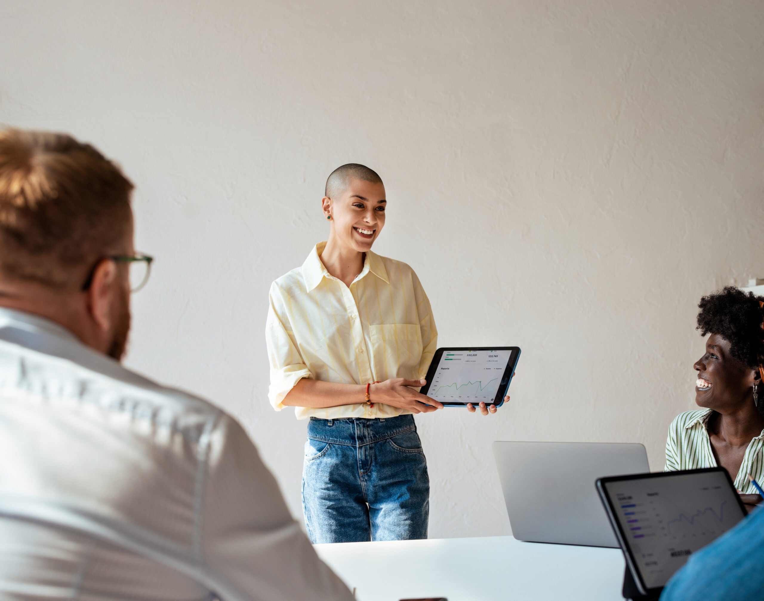 Confident young woman presenting data on a tablet during a business meeting. Team discussing growth and progress in a modern office setting.