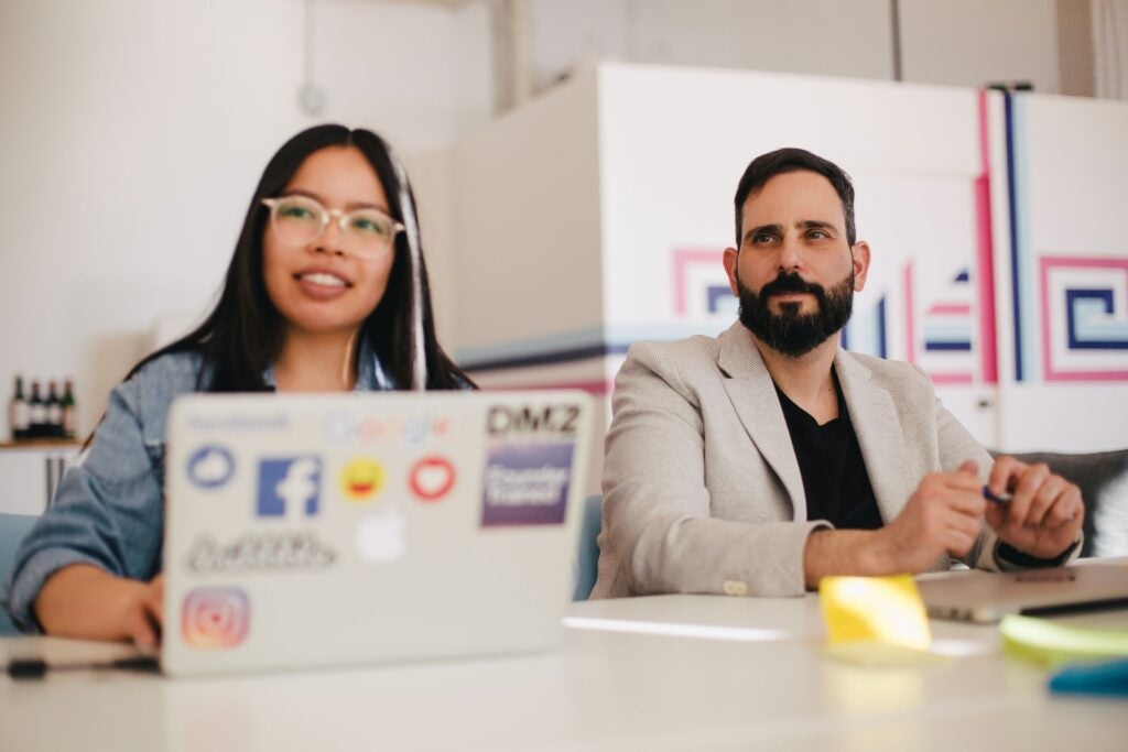 Young man and young woman sitting at a table next to a laptop